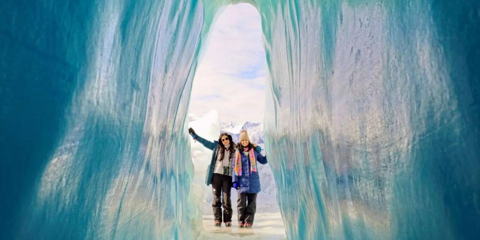 Two visitors standing inside a turquoise ice arch on the Matanuska Glacier