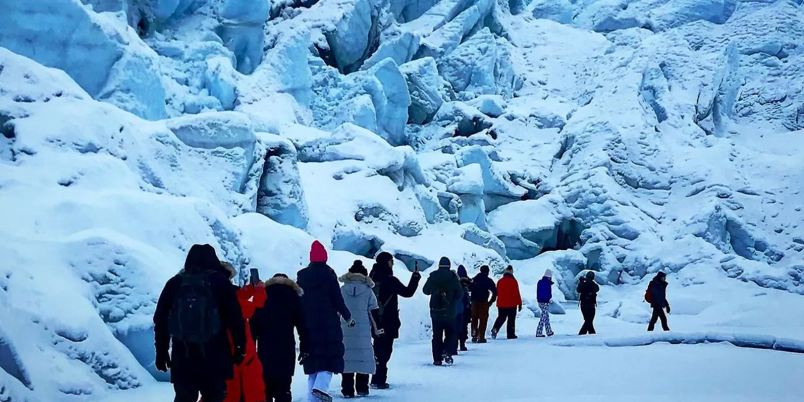 Winter tour group in parkas walking single file into the glacier ice