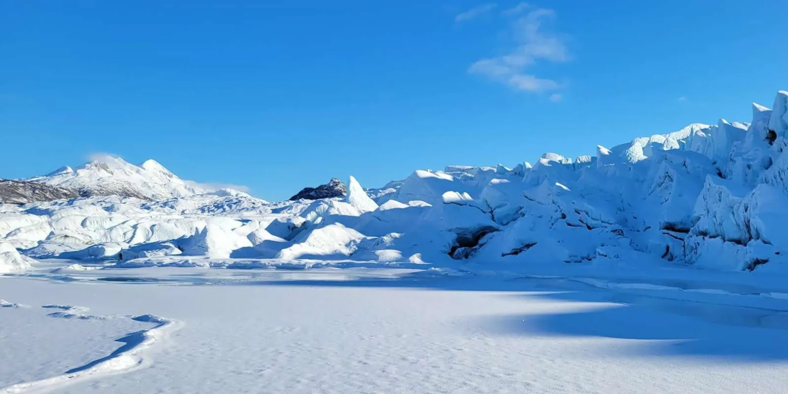 Snow-covered glacier surface under a clear blue winter sky