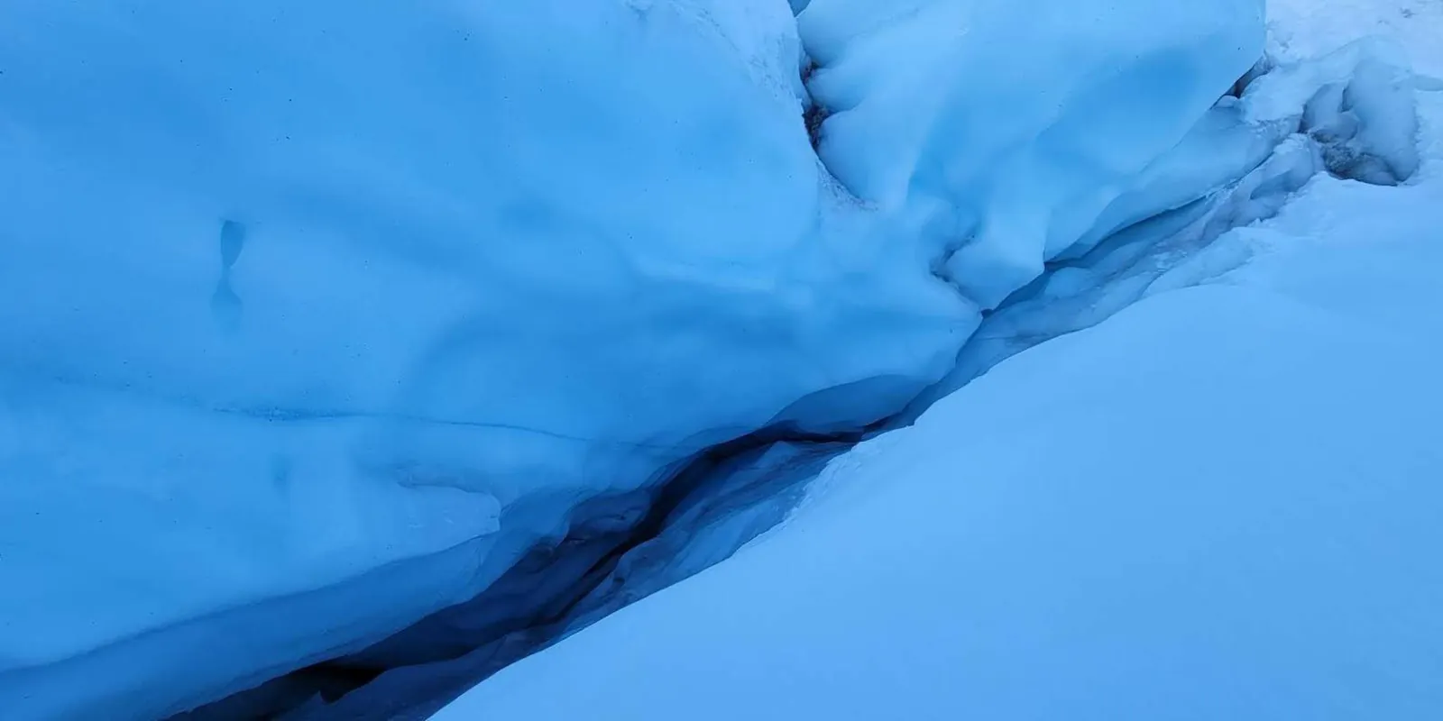 Deep blue crevasse cutting through fresh snow on the glacier
