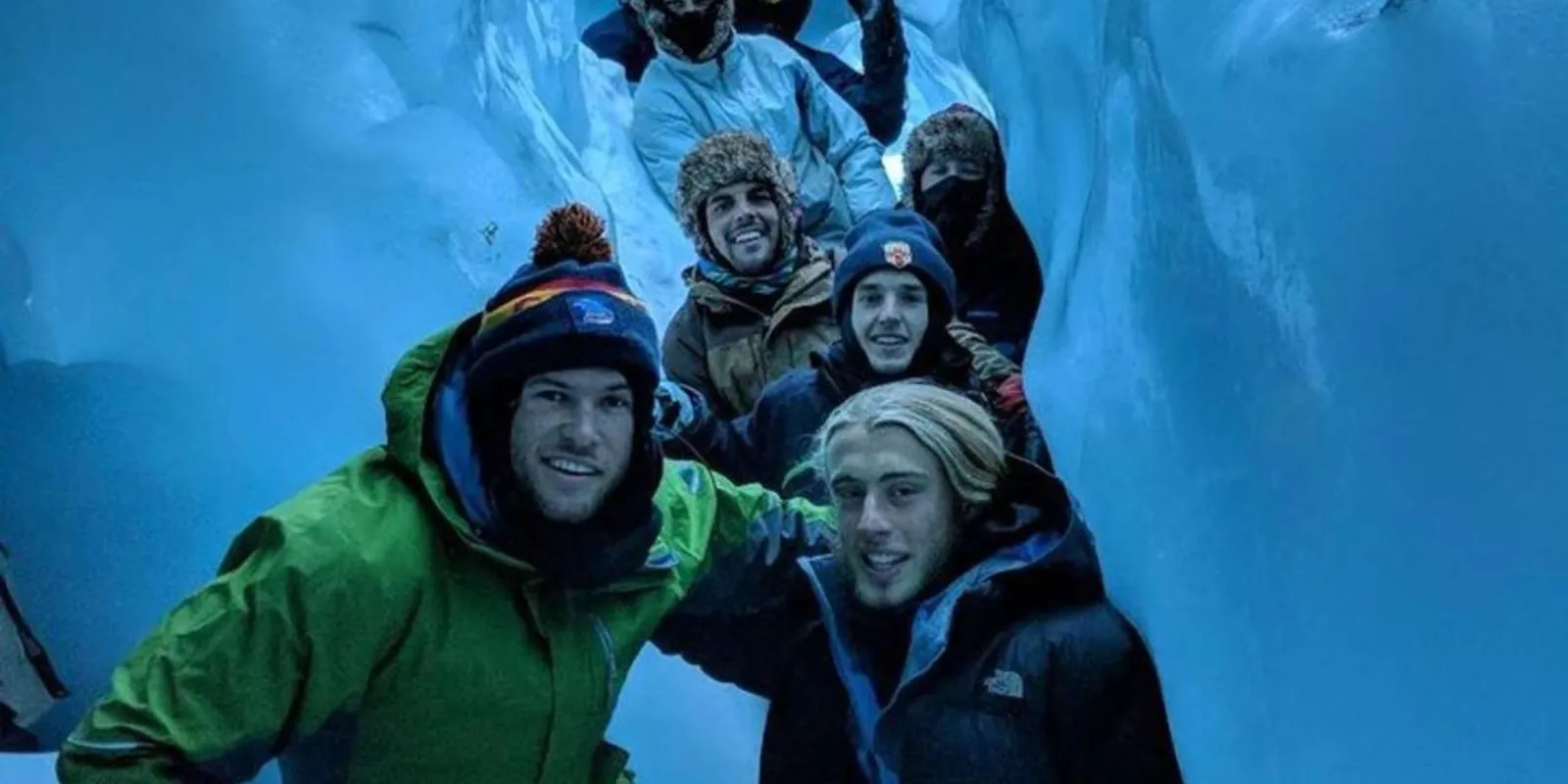 Group of friends smiling inside a blue ice chamber on the glacier