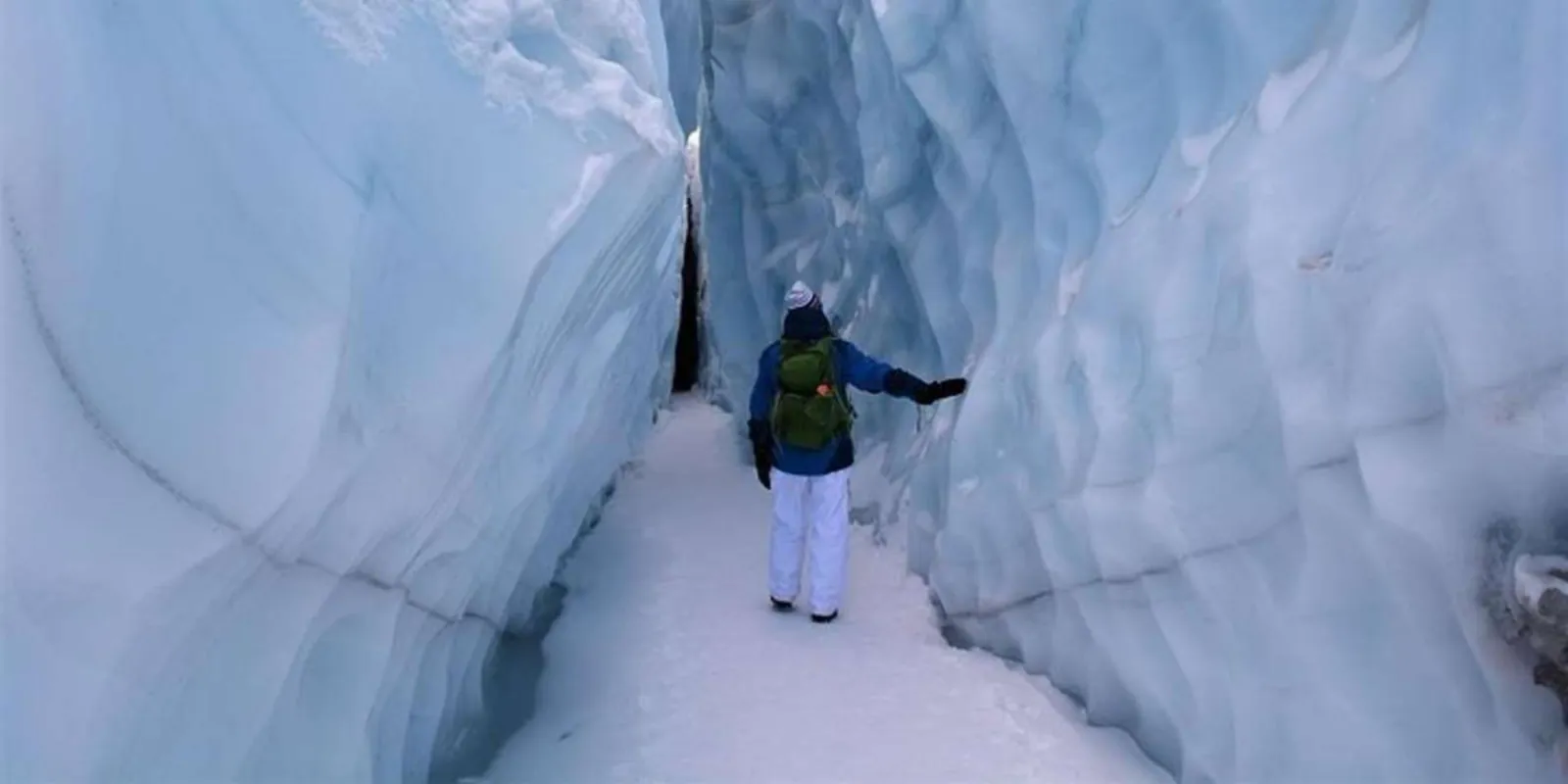 Lone visitor walking a narrow snow-floored corridor between ice walls