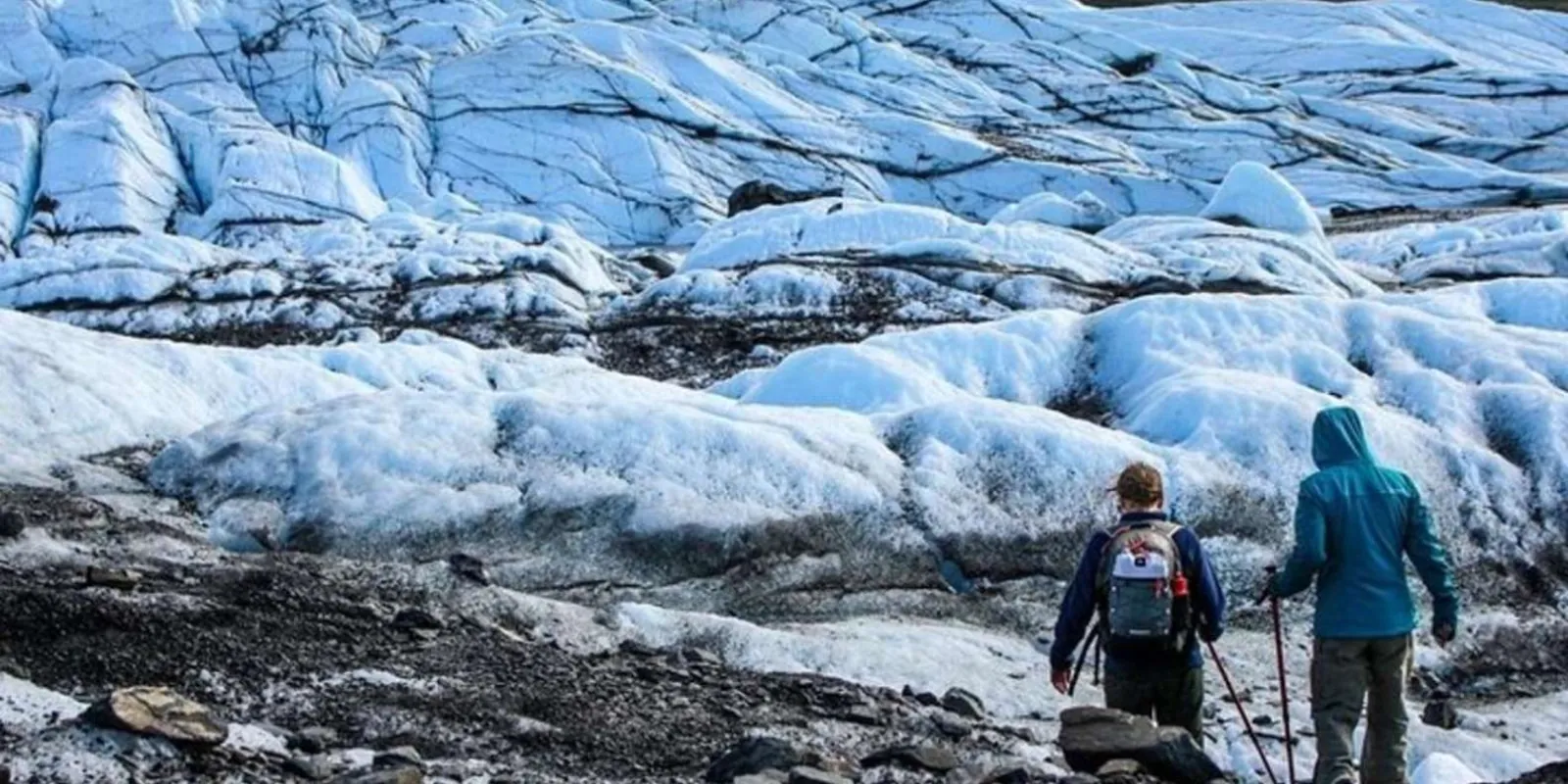 Two hikers with poles crossing the ice below the seracs