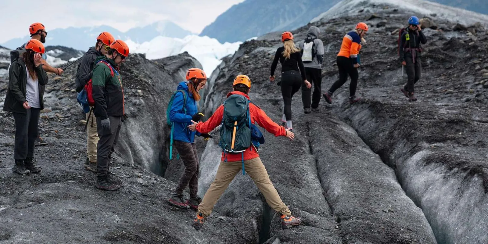 Hiker stepping across a narrow crevasse with the rest of the group behind