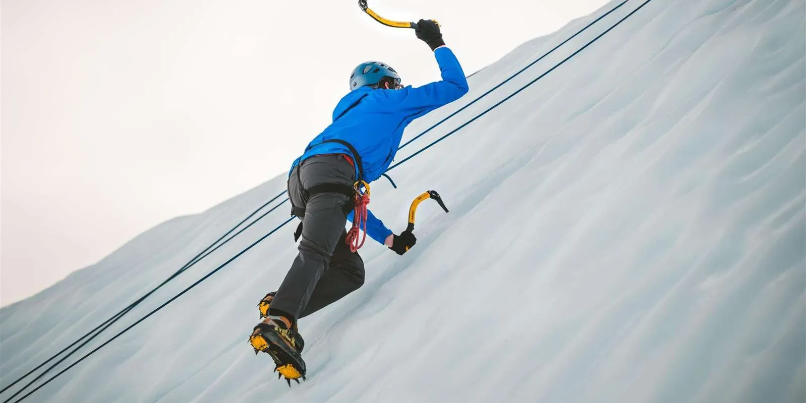 Climber swinging an ice axe high on a blue ice face
