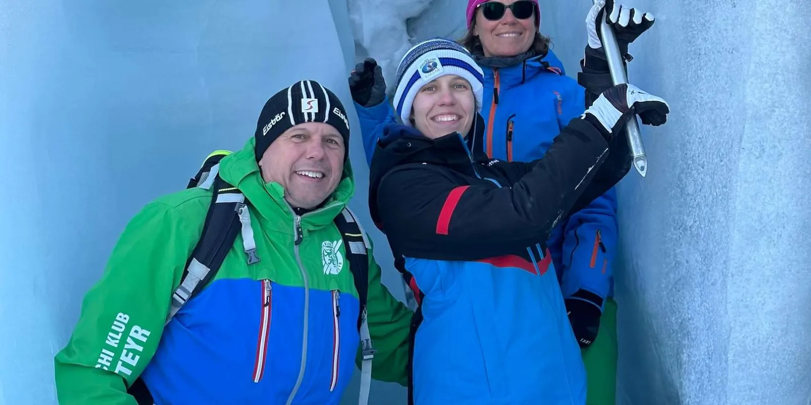 Three guests smiling inside a blue ice alcove