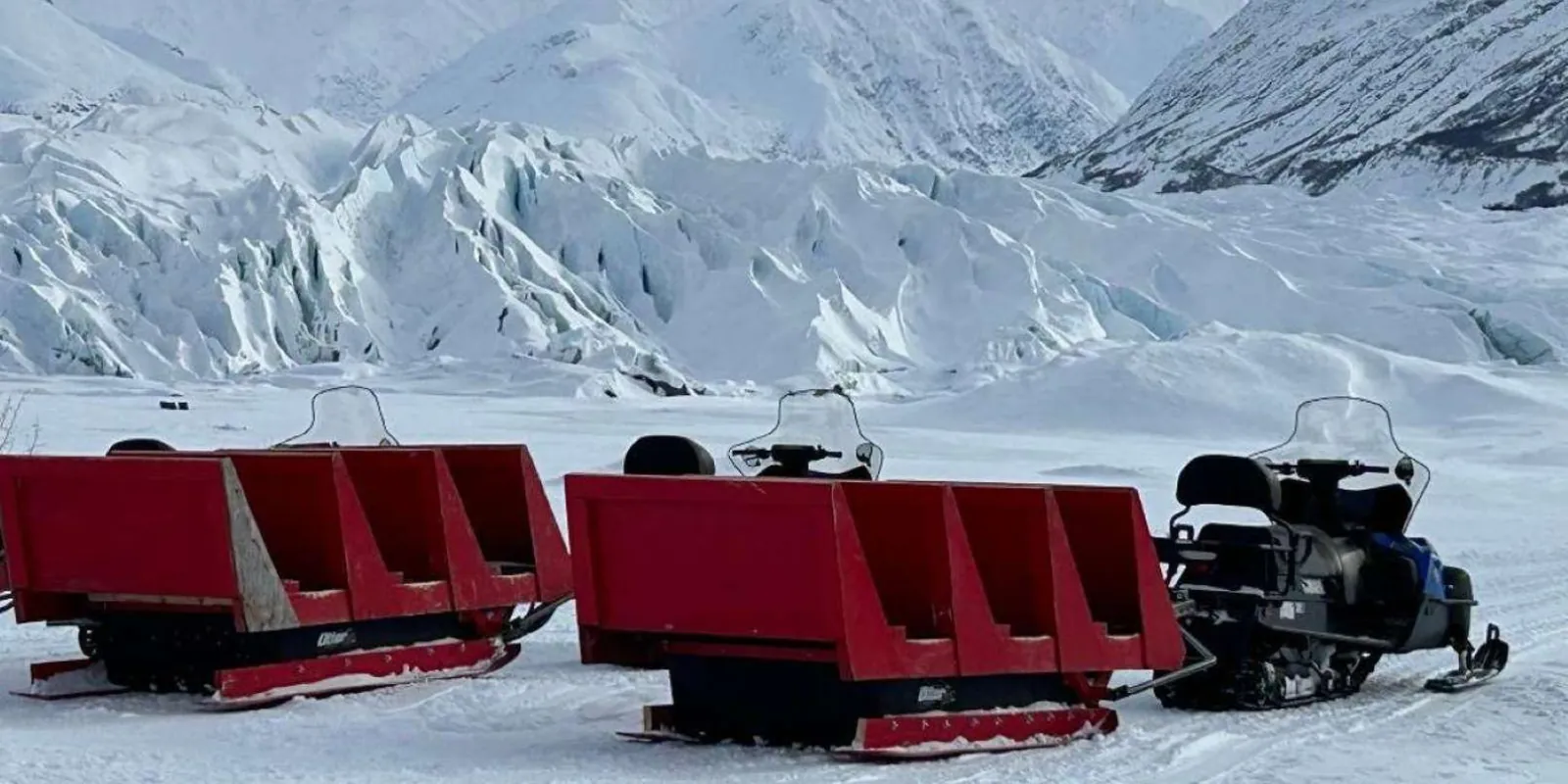 Red snow-machine sleds parked on the ice at the trailhead
