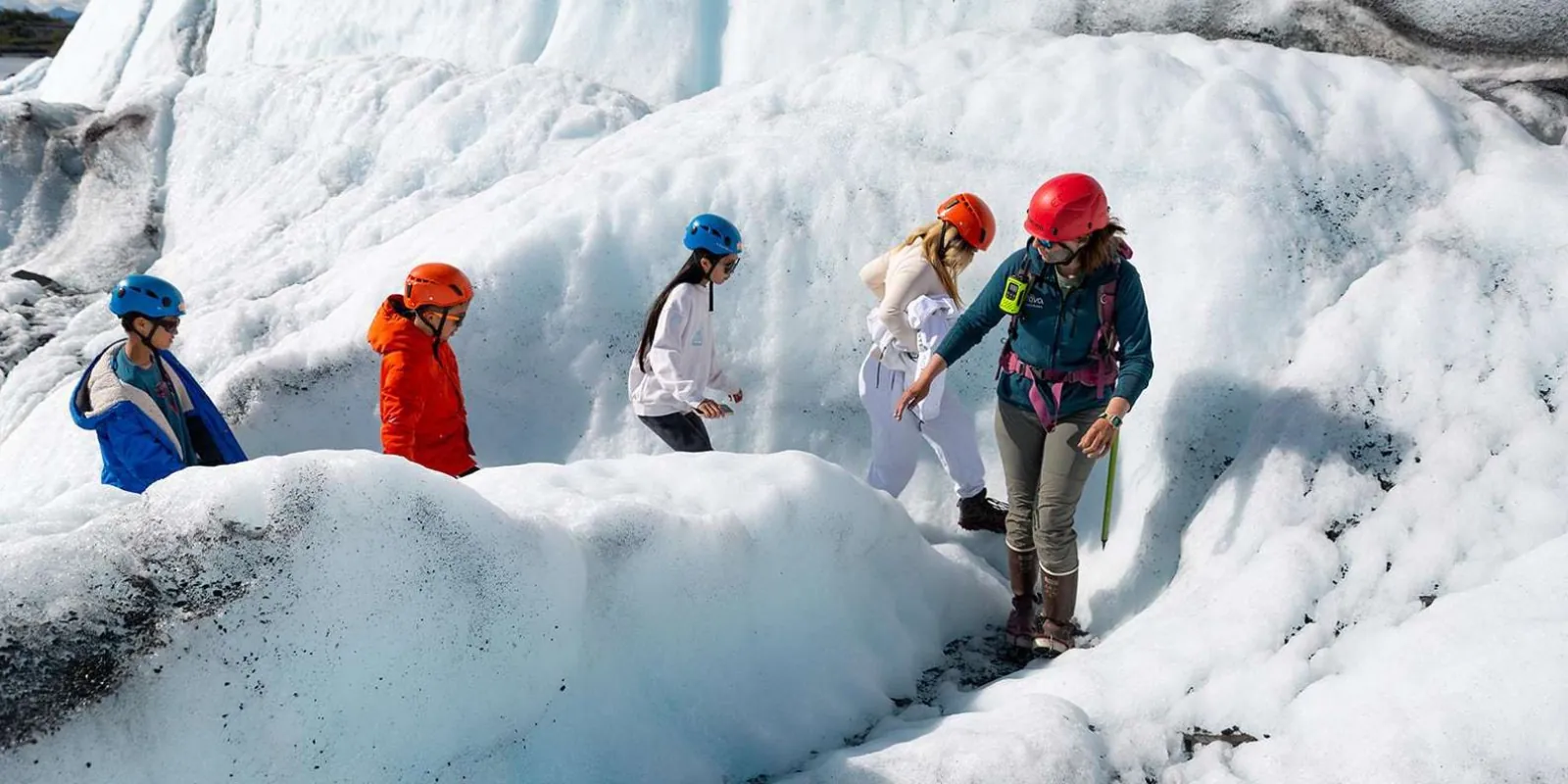 Children and parents in helmets descending a low ice slope