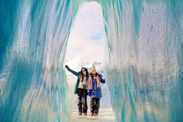 Two visitors standing inside a blue ice cave on the Matanuska Glacier